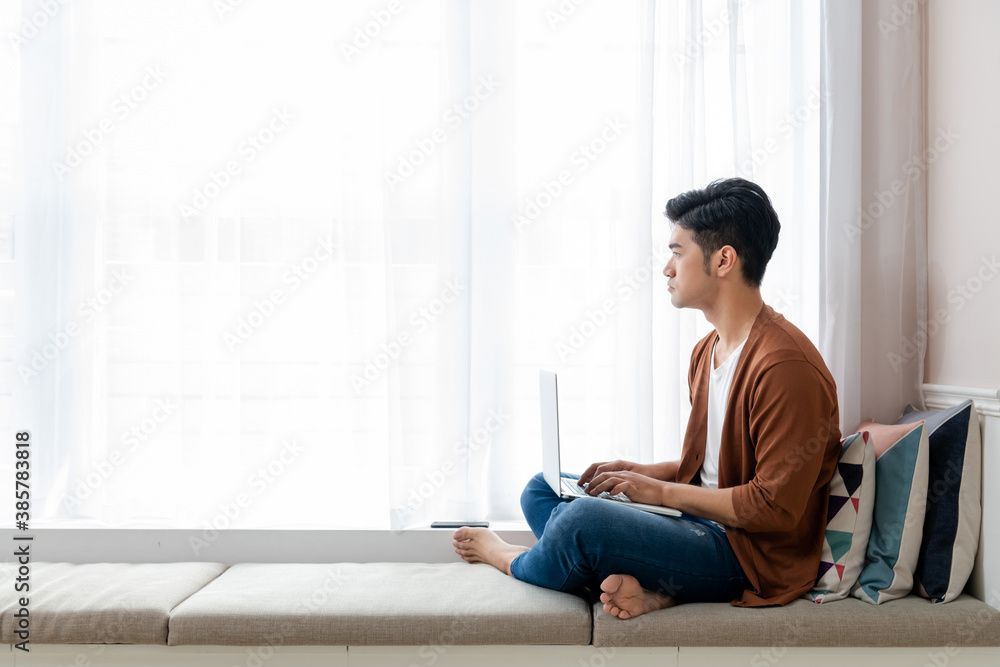A young man working at home, sitting by the window with a laptop (work from home) A young man working at home, sitting by the window with a laptop (work from home)