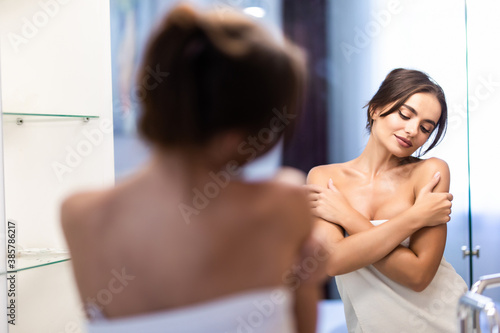 Young woman in bathrobe and towel on head looking at mirror in bathroom