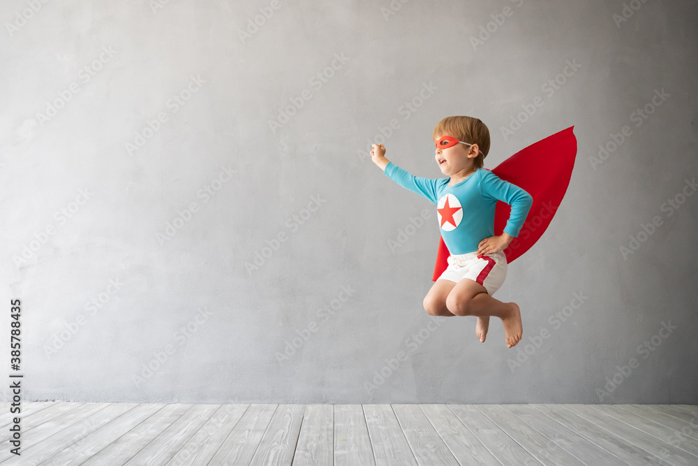 Superhero child jumping against grey concrete background