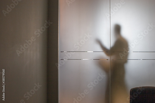 Businessman seen through frosted glass wall at office