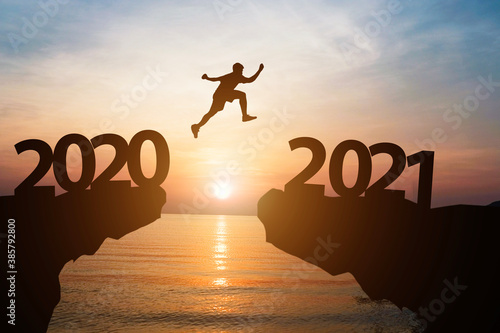 Canvas Print Happy new year 2021 and silhouette concept , Man jumping from 2020 to 2021 with beautiful orange sky and sea