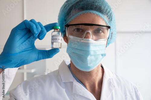 Portrait of female doctor wearing face mask holding a vial bottle with Covid-19 text