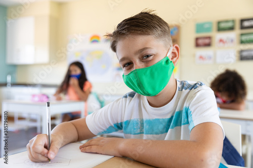 Portrait of boy wearing face mask sitting in class at school