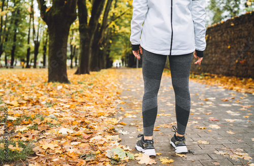 Young fit athletic woman wears modern running clothes standing on the footway before jogging in the autumnal city park. Active running people concept image.