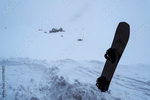 Snowboard in the snow at Balea lake with people and Paltinu cottage in the backgroud. photo