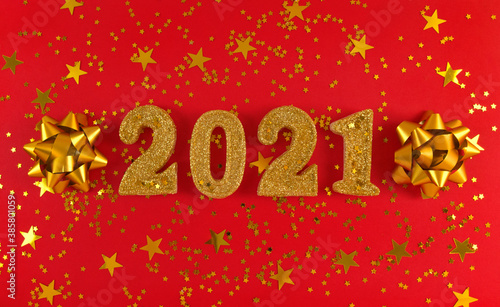 Greeting card of New Year 2021. Golden glittered figures, stars and bows on a red background.