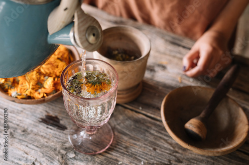 Teapot pouring hot water in herbal tea glass on table