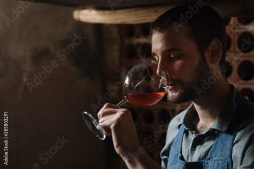 Young bearded man drinking wine from glass at cellar photo