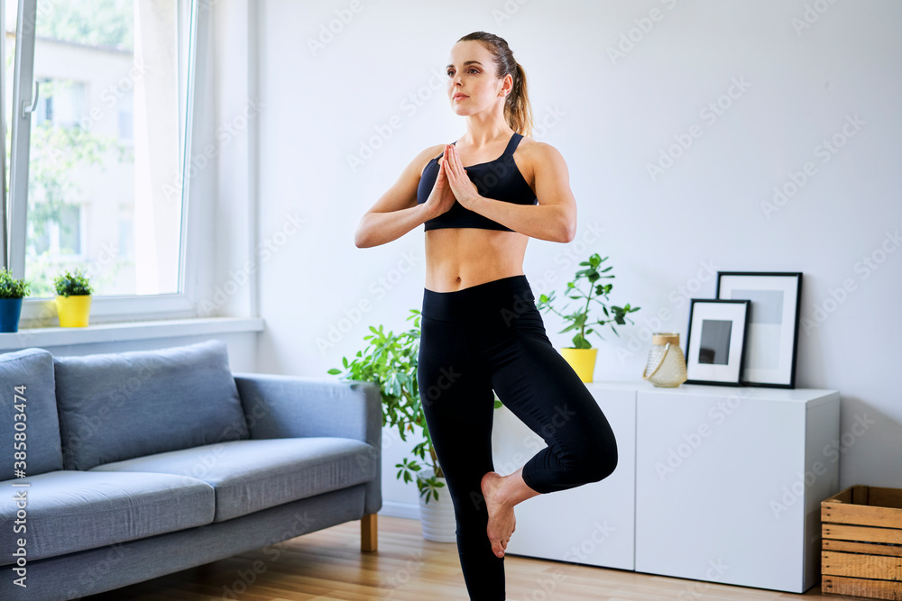 Woman in sports clothing practicing tree pose at home