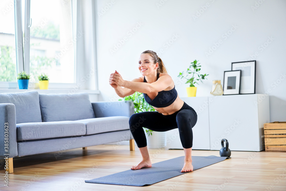 Smiling woman doing squats during home workout Smiling woman doing squats during home workout