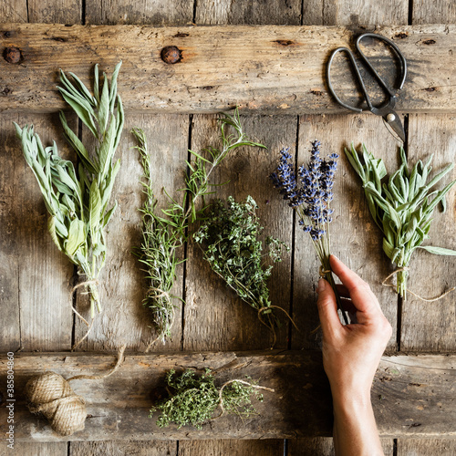 Hand of woman picking up bundled herbs lying on wooden surface