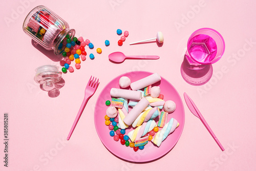 Studio shot of glass of water, jar of candies and plastic plate filled with various sweets photo