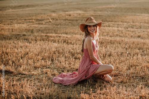 Smiling young woman kneeling in wheat field during sunset photo