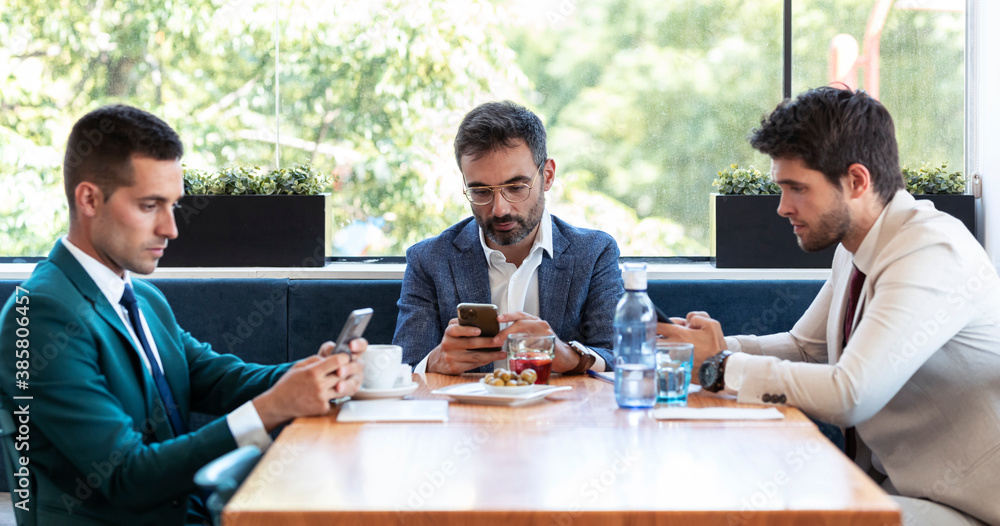 Male business professionals busy in using smart phones during meeting in restaurant Male business professionals busy in using smart phones during meeting in restaurant