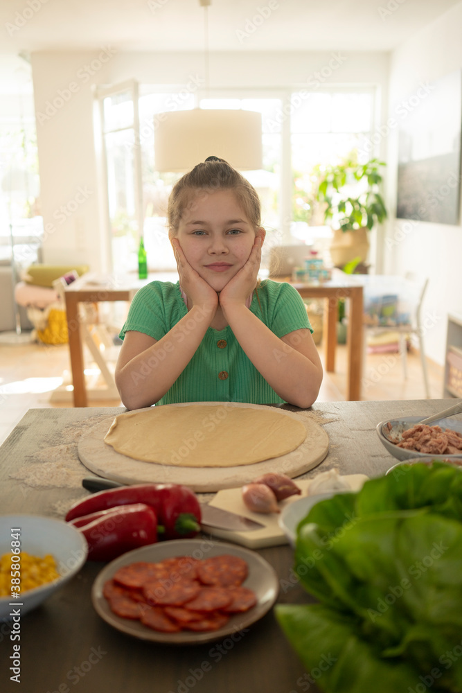 Cute girl sitting by table with pizza ingredients at home Cute girl sitting by table with pizza ingredients at home