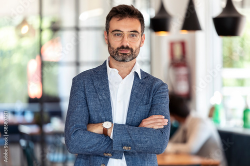 Confident businessman standing with arms crossed in restaurant photo