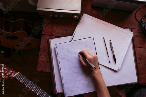 Young woman writing in book at table while practicing guitar