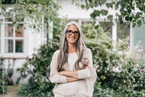 Portrait of smiling woman with long grey hair wearing spectacles standing in the garden photo