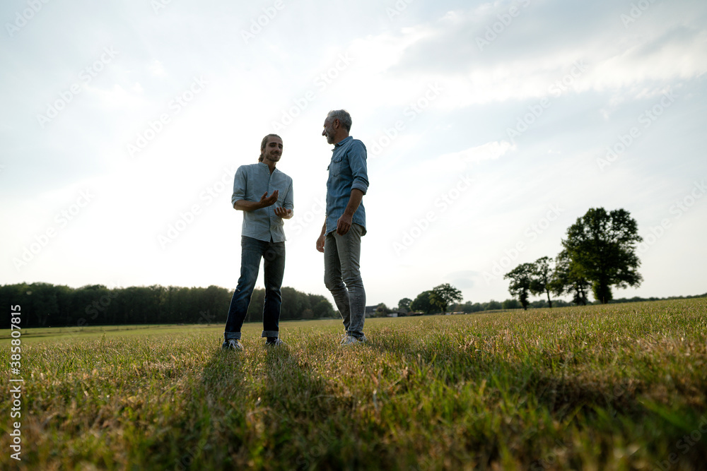 Father and adult son standing on a meadow in the countryside Father and adult son standing on a meadow in the countryside