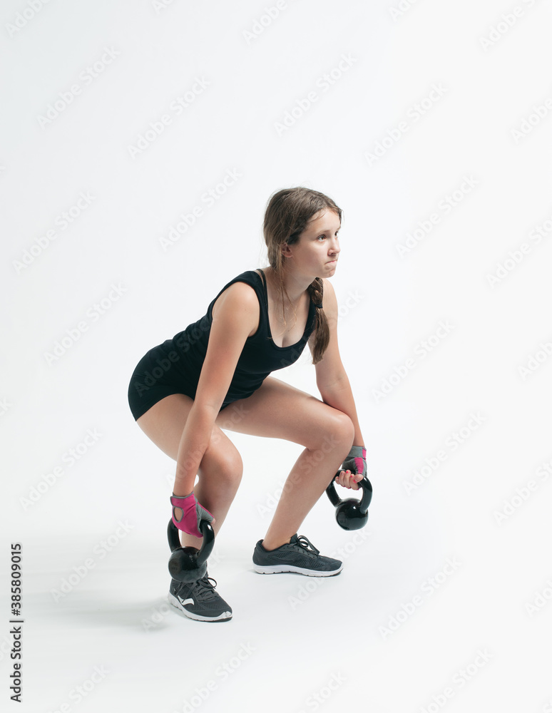 teenage girl during the squat with the kettlebells over the white background