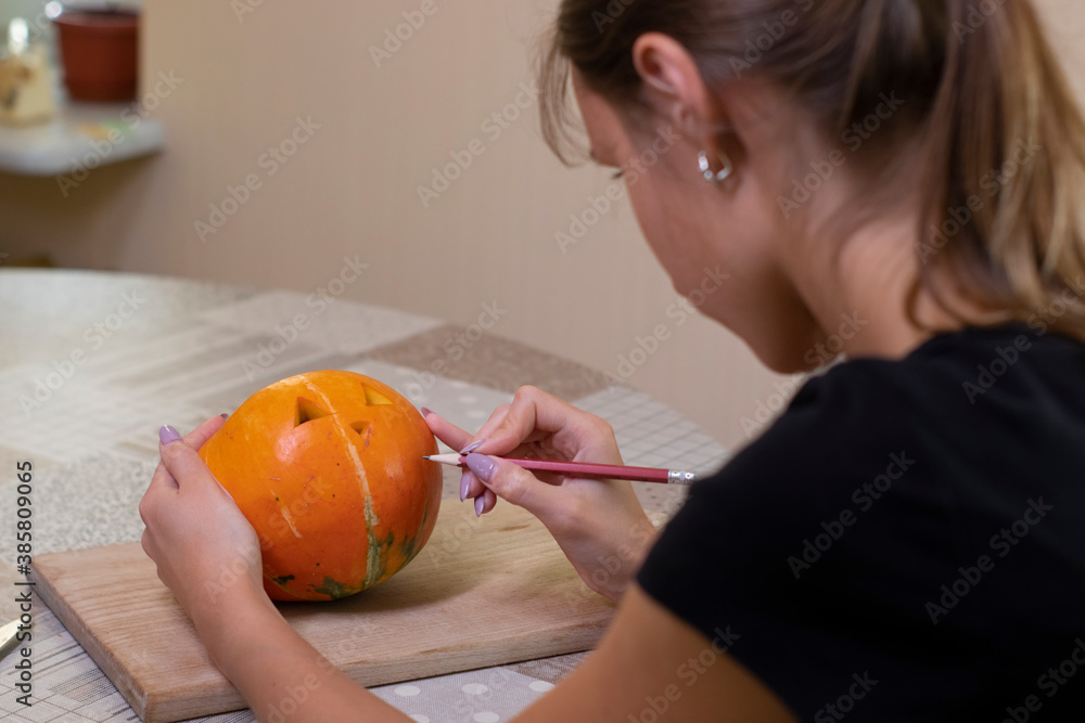 Fototapeta premium the process of making a Halloween pumpkin. drawing a layout by a brunette girl. horror theme and Hallowe'en. 