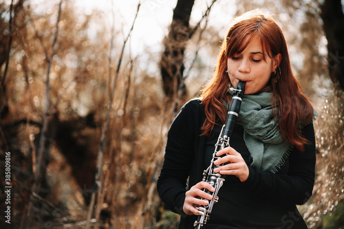 Beautiful redhead woman practicing clarinet in forest photo