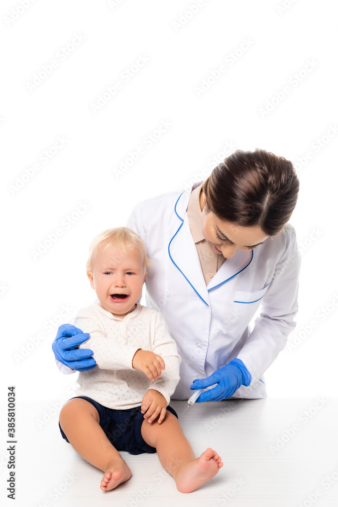 Doctor holding syringe near crying toddler boy isolated on white Doctor holding syringe near crying toddler boy isolated on white
