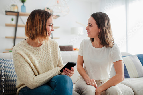 Smiling friends talking while sitting on sofa at home photo