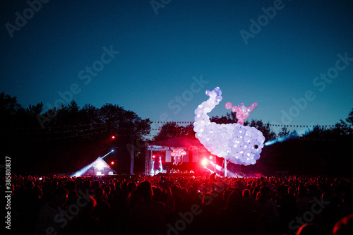 Whale made of purple balloons floating over crowd of people having fun during night music festival