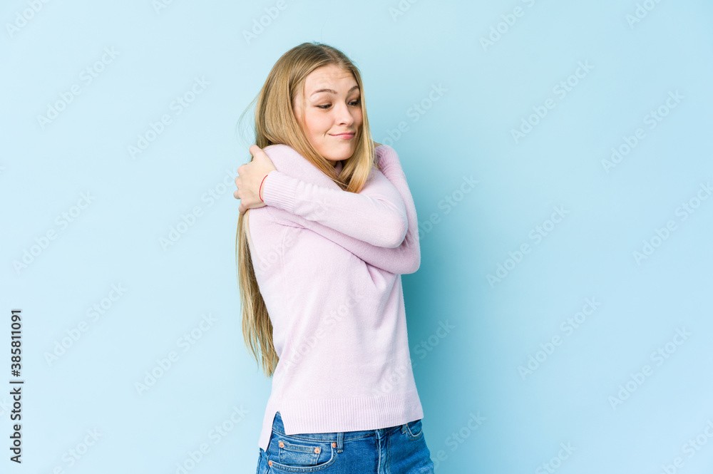 Young blonde woman isolated on blue background hugs, smiling carefree and happy. Young blonde woman isolated on blue background hugs, smiling carefree and happy.
