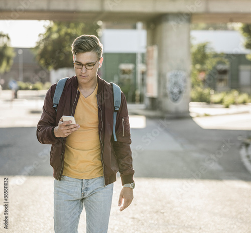 Young man using smart phone while walking on street in city photo