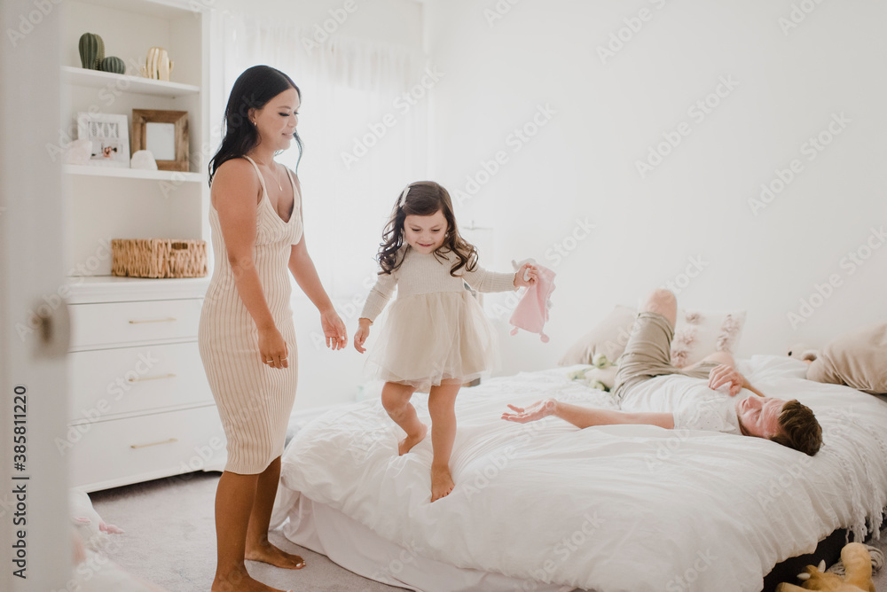Smiling parents looking at daughter standing on bed at home Smiling parents looking at daughter standing on bed at home