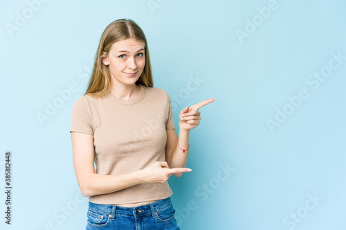 Young blonde woman isolated on blue background shocked pointing with index fingers to a copy space.