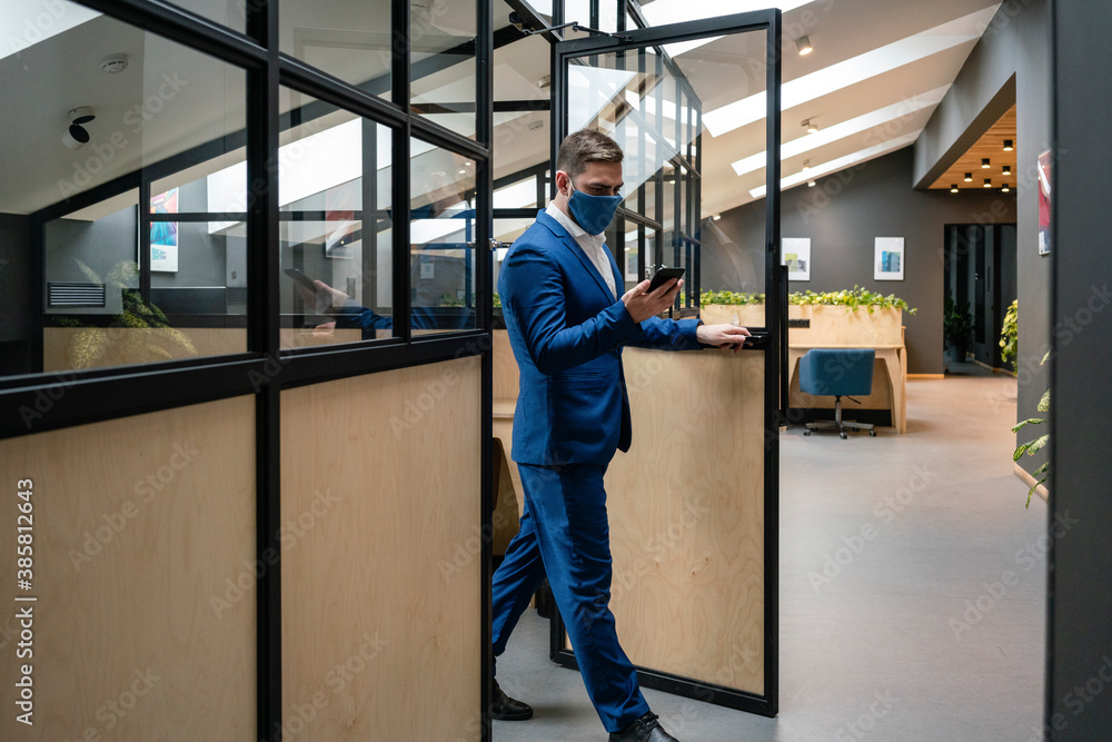 Businessman wearing protective face mask while walking out of cubicle at creative office during coronavirus pandemic Businessman wearing protective face mask while walking out of cubicle at creative office during coronavirus pandemic