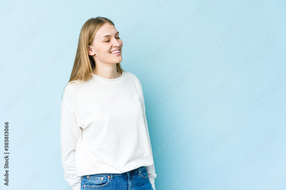 Young blonde woman isolated on blue background relaxed and happy laughing, neck stretched showing teeth. Young blonde woman isolated on blue background relaxed and happy laughing, neck stretched showing teeth.