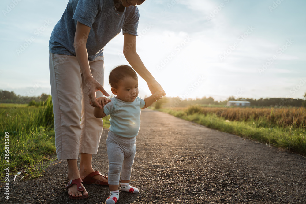 Fototapeta premium mother help her baby to walk her first step on country road