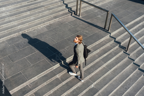 Male entrepreneur with bag moving up on staircase while looking away in downtown during sunny day photo