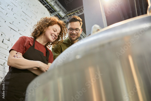 Man and woman working in craft brewery looking into tank photo