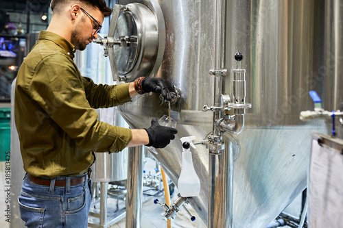 Man working in craft brewery tapping beer from tank photo