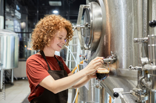 Woman working in craft brewery tapping beer from tank photo