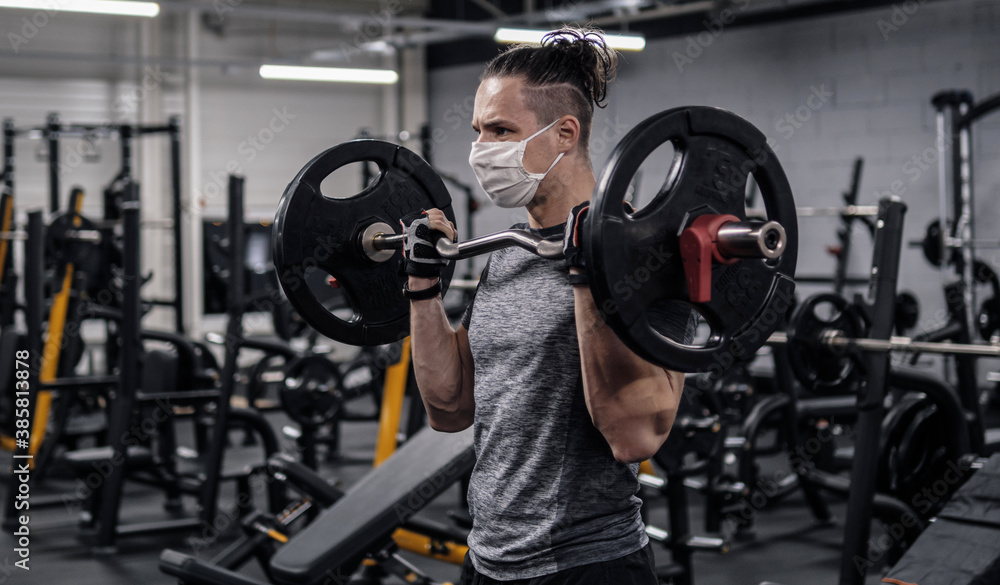 Obraz premium Pandemic gym - man working out with protective face mask during coronavirus outbreak