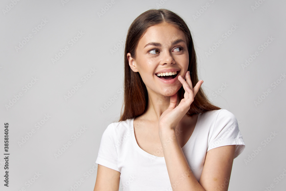 Smiling woman holding her hand near her face and looking to the side on a light background Smiling woman holding her hand near her face and looking to the side on a light background