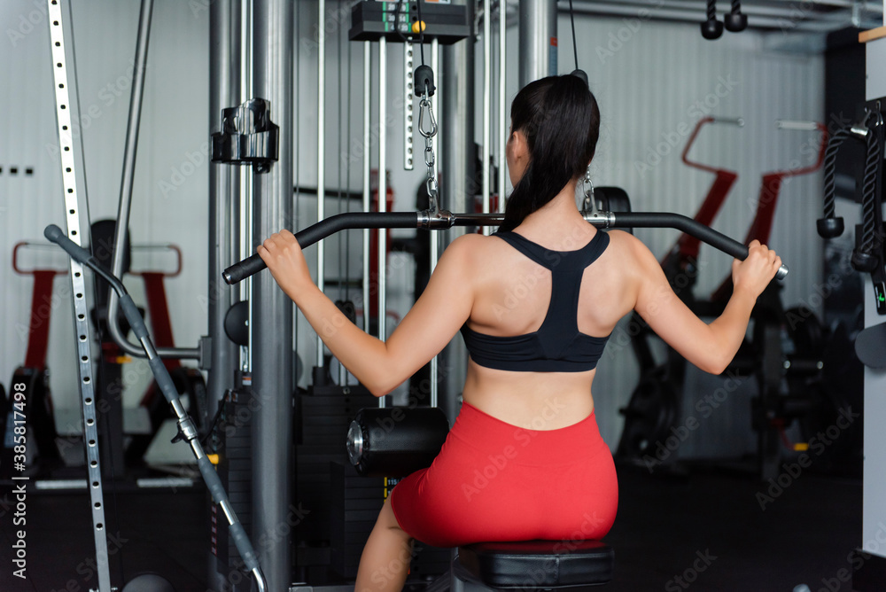 Fototapeta premium Back view of young woman training arms on gym machine