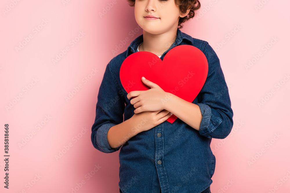 cropped view of boy holding heart shape paper cut on pink cropped view of boy holding heart shape paper cut on pink