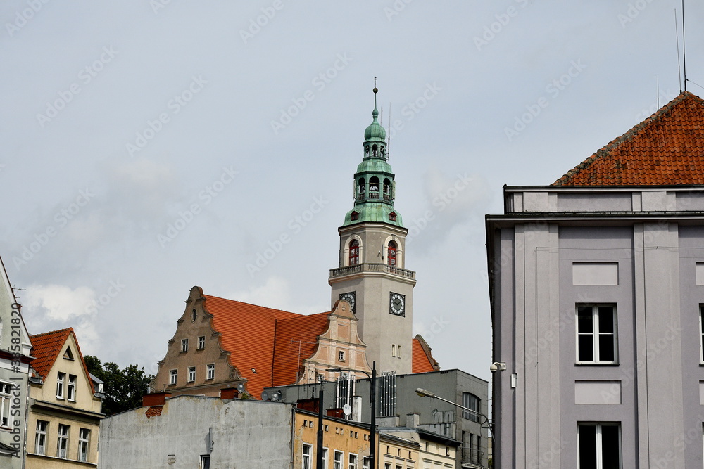 View of a tall tower of the town hall of a Polish city surrounded with block of flats and other habitable units seen on a warm yet cloudy summer day in the middle of a Polish square