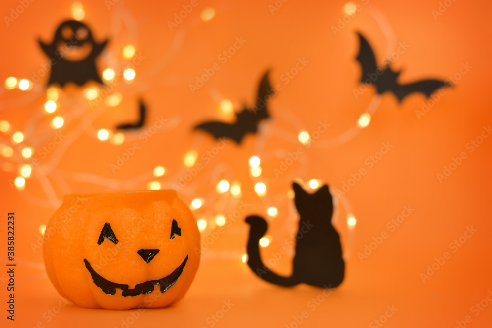 Happy Halloween! Pumpkin, bats, cat, ghost on an orange background and a glowing bokeh background.