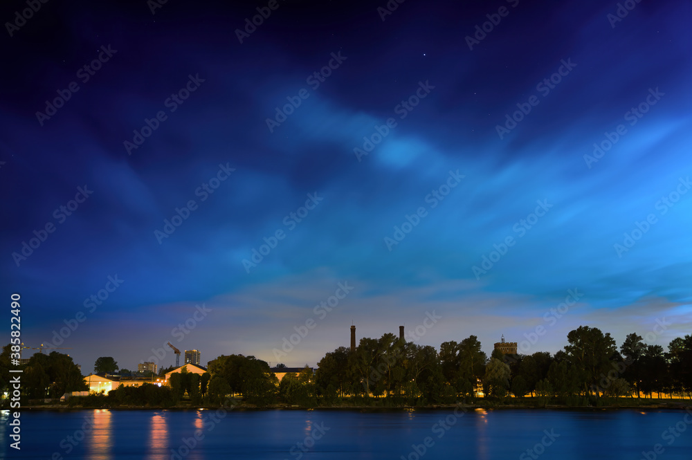 Starry sky with floating clouds over the city park with trees.