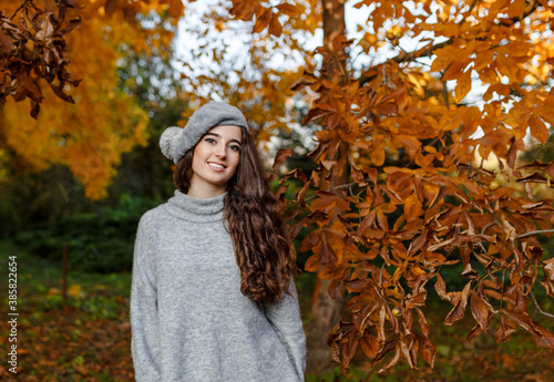 Attractive stylish girl with curly hair walking in park dressed in warm grey autumn trendy fashion, wearing beret hat.