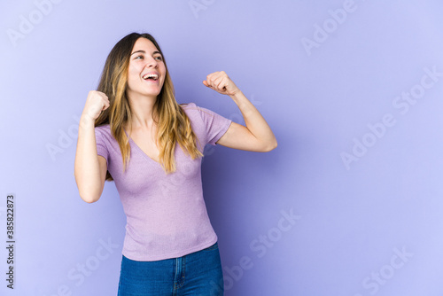 Young caucasian woman isolated on purple background raising fist after a victory, winner concept.