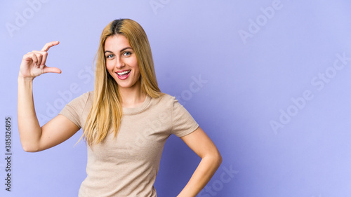 Young blonde caucasian woman holding something little with forefingers, smiling and confident.